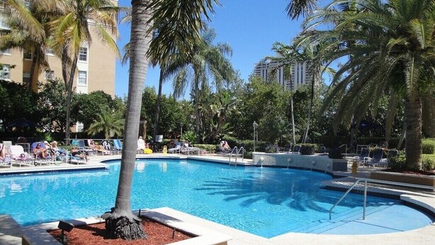 A swimming pool surrounded by palm trees and lounge chairs, with a clear blue sky above.