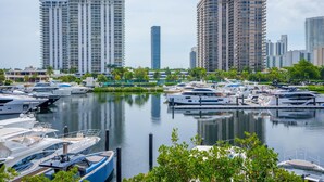 A marina with multiple yachts docked, surrounded by high-rise buildings and greenery.