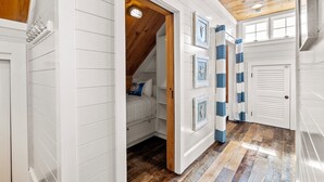 Ein Flur mit weißen Wandverkleidungen, einer Holzbalkendecke und einem durch eine offene Tür sichtbaren geneigten Dach.