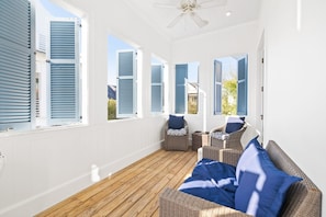 A sunlit room with a wooden floor, wicker furniture, and large windows with shutters. - Providence Cottage in Rosemary Beach, 3rd tier home from Gulf with Gulf view (Rosemary Beach)