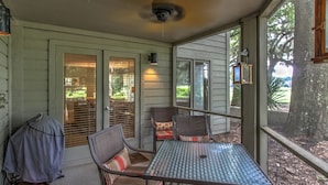 A covered patio with a metal table and chairs, a grill, and a view of the backyard.