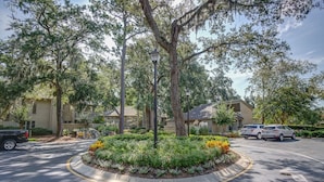 A parking lot with a landscaped flower bed, trees, and a building in the background.