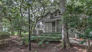 A two-story house with a front porch, surrounded by dense trees and a well-maintained garden.