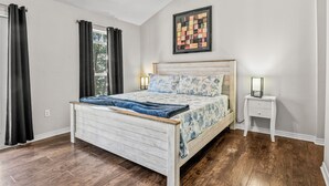 Quarto com cama de madeira, mesa de cabeceira, ventoinha no teto e janela com cortinas.