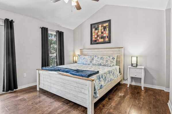 A bedroom with a wooden bed, a nightstand, a ceiling fan, and a window with curtains.