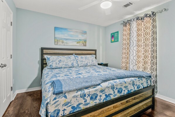 Un dormitorio con cama, un cuadro en la pared, una mesita de noche y una cortina estampada.