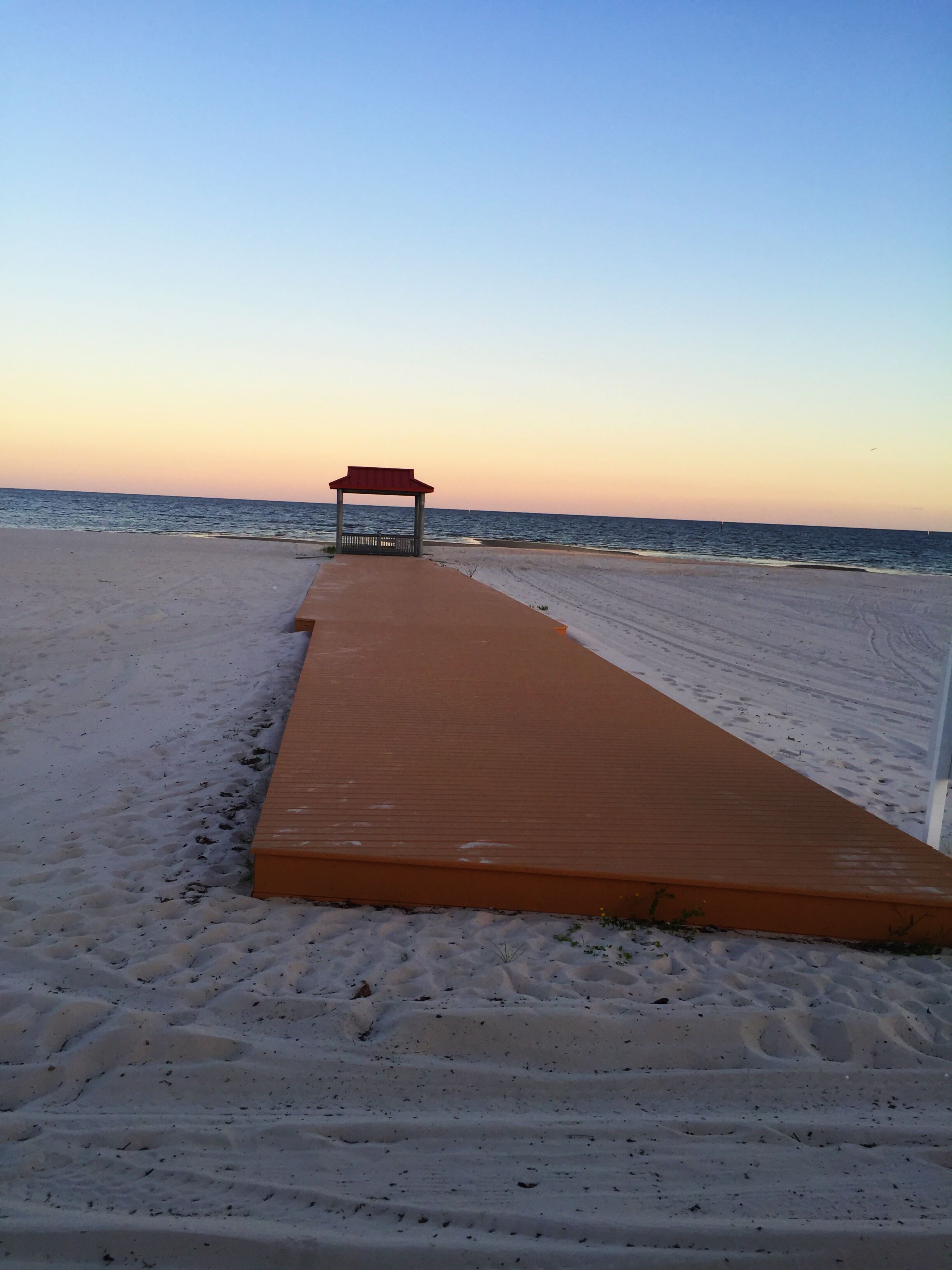 A wooden pathway leading to a beach with a small shelter.