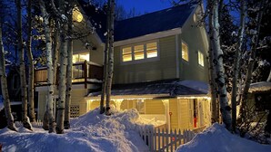 Una casa de dos pisos con un camino cubierto de nieve y una valla de piquetes blancos.
