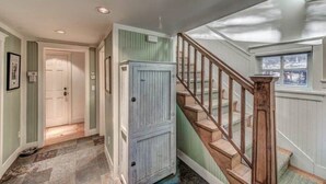 Un pasillo con una escalera de madera, una puerta y una ventana.