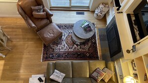 Una sala de estar acogedora con un sofá de cuero marrón, un reposapiés a juego, una alfombra estampada y un televisor.