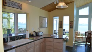 A kitchen with a large island, wooden cabinets, a sink, and a view of the outdoors. - Miracle Ridge - Beautiful, Private Home Overlooking Kachemak Bay & Cook Inlet (Homer)
