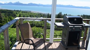 A deck with a grill and a chair overlooking a lake and mountains. - Miracle Ridge - Beautiful, Private Home Overlooking Kachemak Bay & Cook Inlet (Homer)