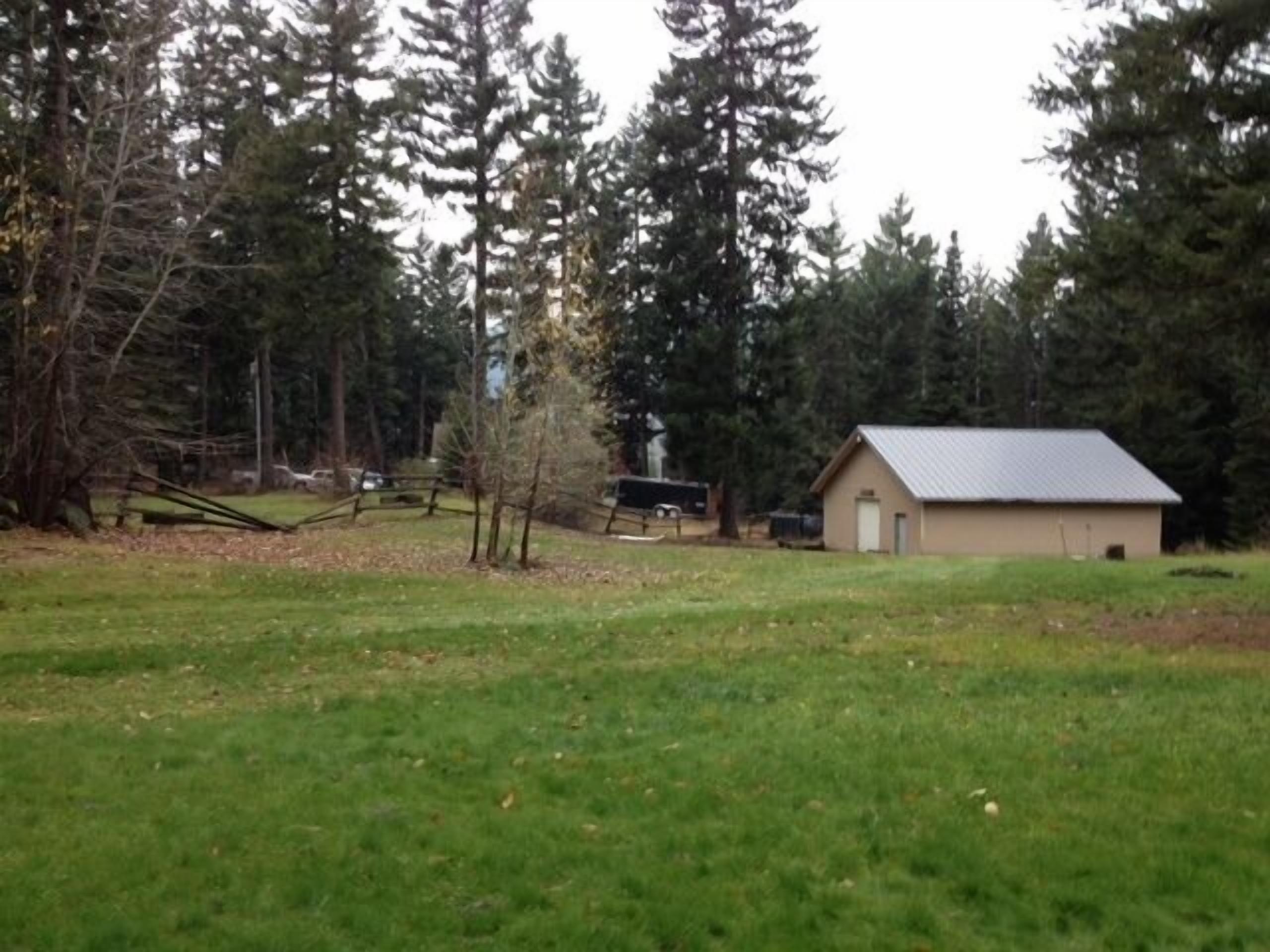 A small building with a sloped roof, surrounded by a grassy field and dense trees.