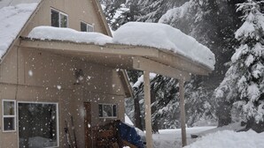 Una casa con porche cubierto y tejado cubierto de nieve.