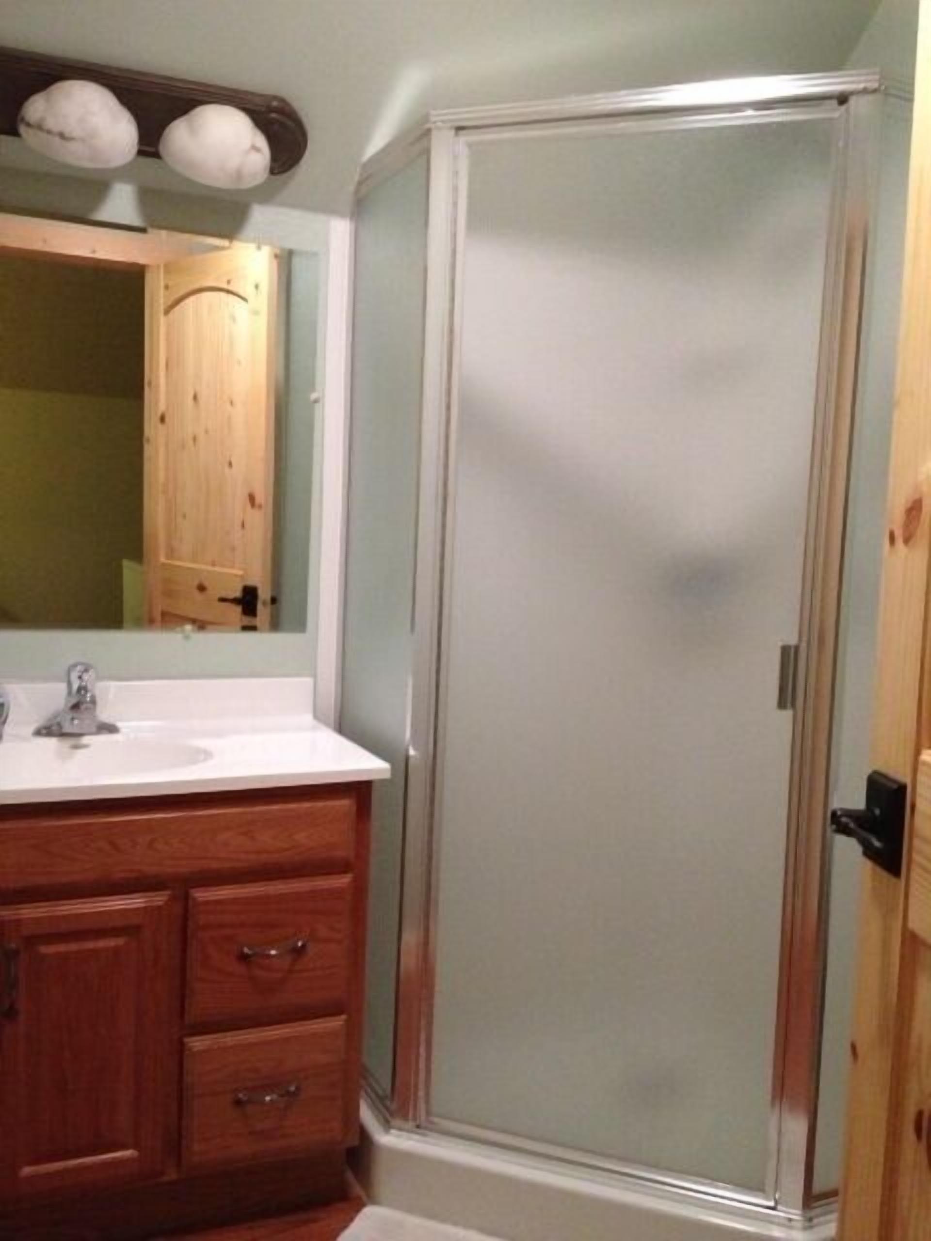 Un baño con tocador de madera, lavamanos blanco y cabina de ducha de vidrio.