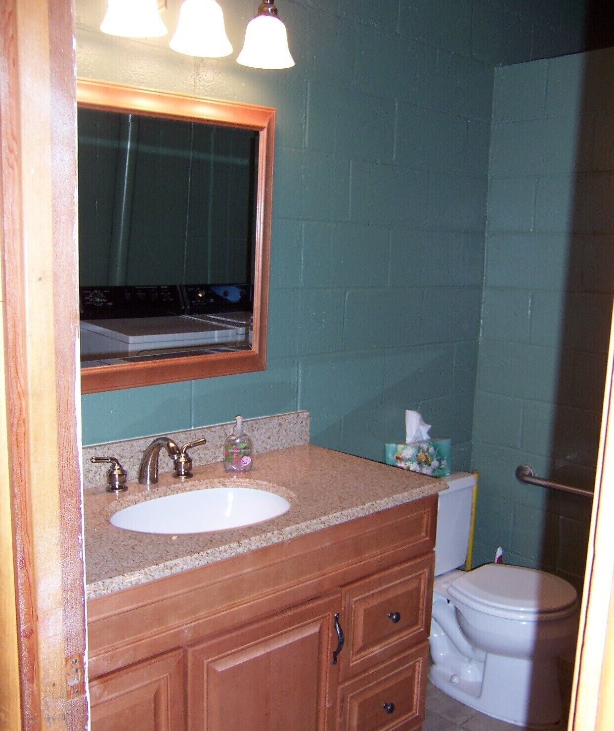 A bathroom with a white sink, wooden vanity, a mirror, and a toilet.
