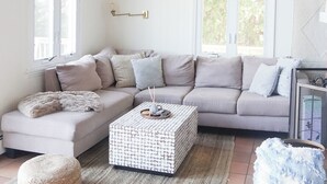 Un saló acollidor amb un sofà seccional, un otomà estampat i un ventilador de sostre rústic.