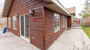 A wooden building with a number '110' on the side, a covered porch, and a small outdoor seating area. - Fantastic House In Grand Marais! Walking Distance To Downtown! (Grand Marais)