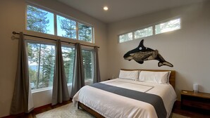 A bedroom with a large bed, multiple windows, and a wall-mounted shark artwork. - Water Views from this New Northwest Modern Home w/ Hot Tub (Eastsound)