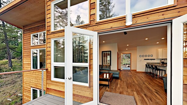 A modern log cabin with a spacious interior, including a living area, kitchen, and a balcony with a wooden deck. - Water Views from this New Northwest Modern Home w/ Hot Tub (Eastsound)