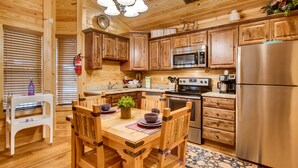 Una cocina de madera con una mesa de comedor, sillas, microondas, estufa, refrigerador y armarios de madera.