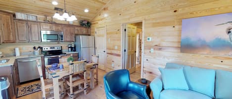 Un interior de cabaña acogedor, con paredes de madera, una cocina con electrodomésticos modernos, un sillón de cuero azul y un sofá azul claro.