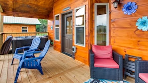 Una terraza de madera con mobiliario exterior, un jacuzzi y una zona cubierta con puerta y ventanas.