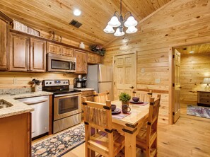 A cozy wooden cabin kitchen with a dining area, featuring a stove, microwave, refrigerator, and wooden cabinets.