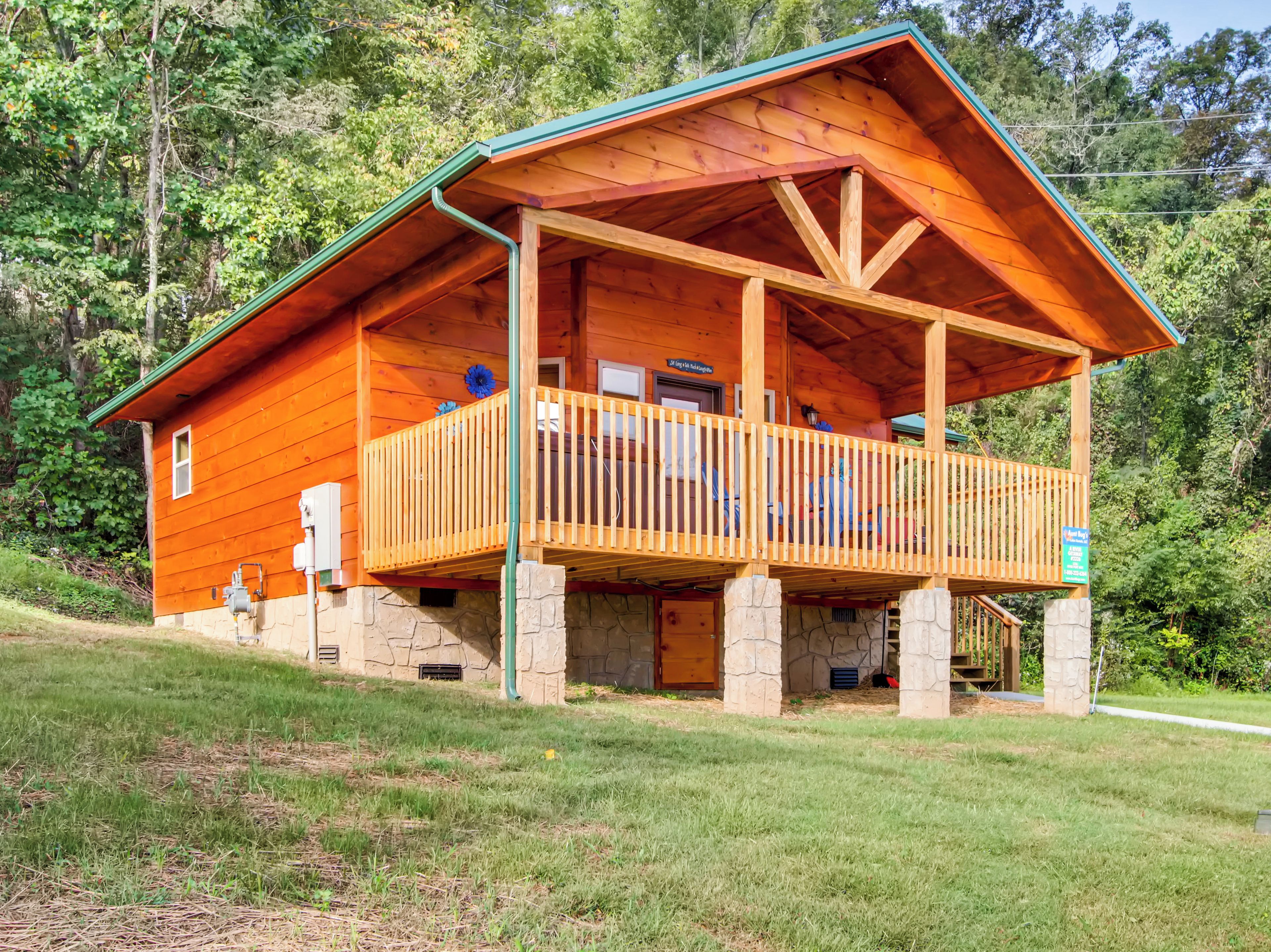 A wooden cabin with a balcony, stone foundation, and a green roof.