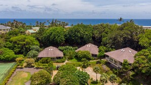 A residential area with three houses surrounded by lush greenery and a tennis court. - Poipu Crater 26 | Tropical Retreat w/ Pool, Lanai & Garden Views (Koloa)