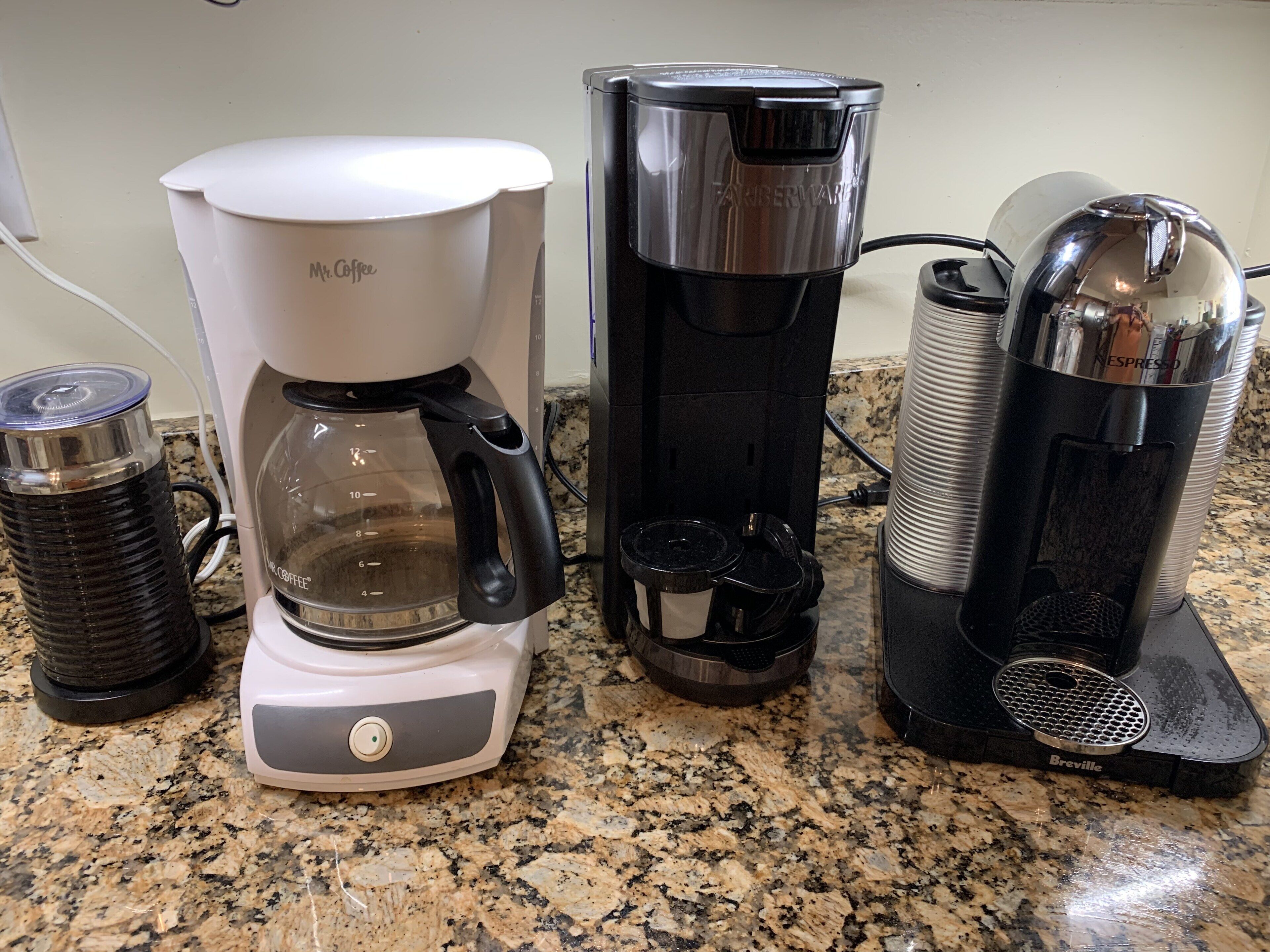 A coffee maker, a water dispenser, and a coffee machine on a granite countertop.