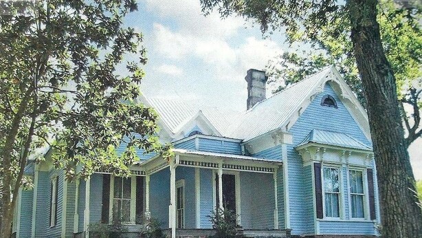 Ein blaues Haus mit Veranda, Schornstein und gepflegtem Rasen.