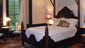 Ein Bett mit Baldachin, ein Nachttisch mit Lampe, ein Sessel und Blick ins Grüne durch das Fenster.