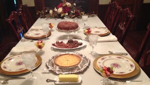 Ein festlich gedeckter Esstisch mit Tellern, Gläsern, Besteck und verschiedenen Speisen, darunter ein Kuchen und eine Obstschale.
