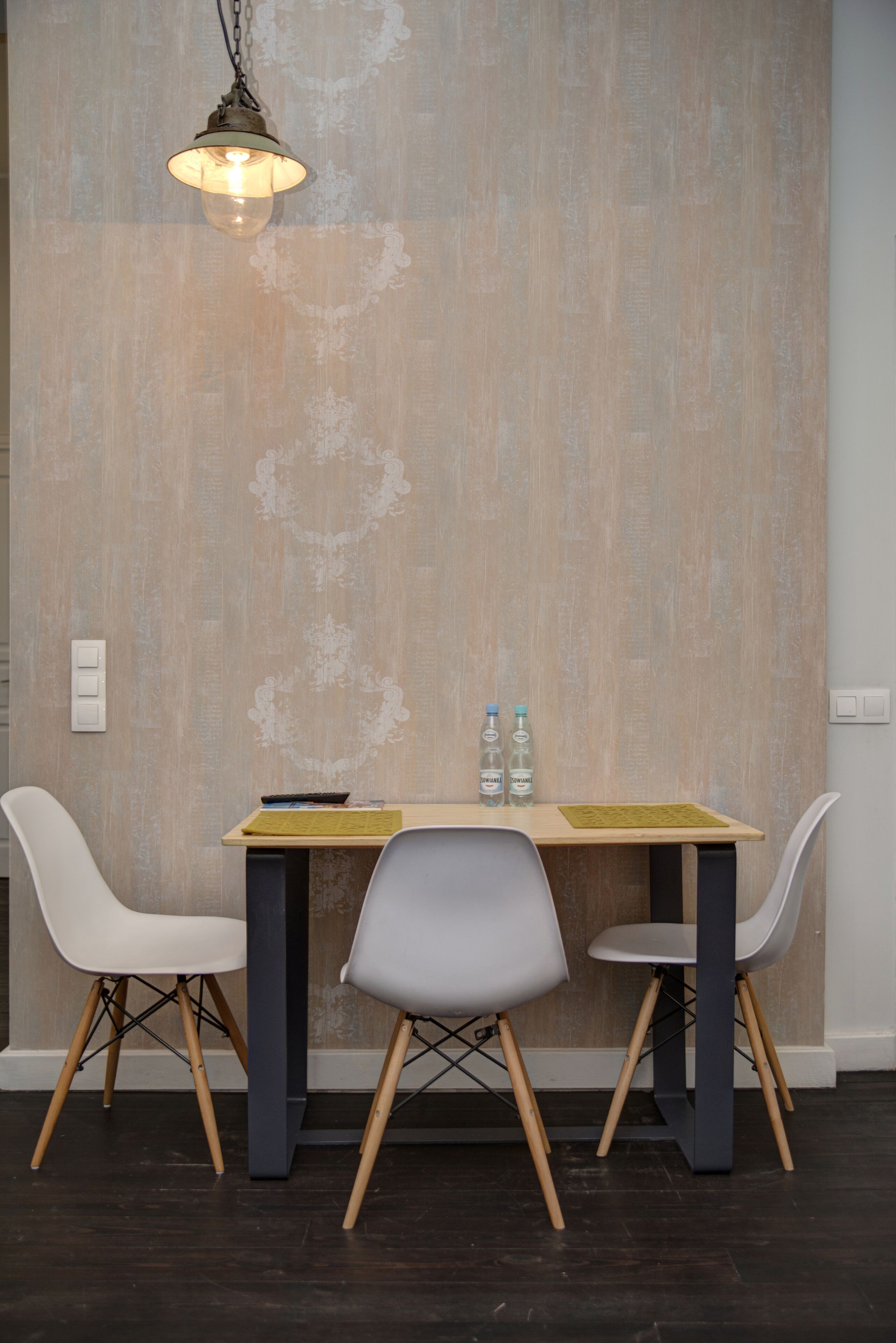 A dining area with a table, two chairs, a hanging light fixture, and a wall with a textured pattern.