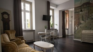A living room with a sofa, a dining table with chairs, a television, and a clock on the wall. - Good Time Aparthotel (Lodz)