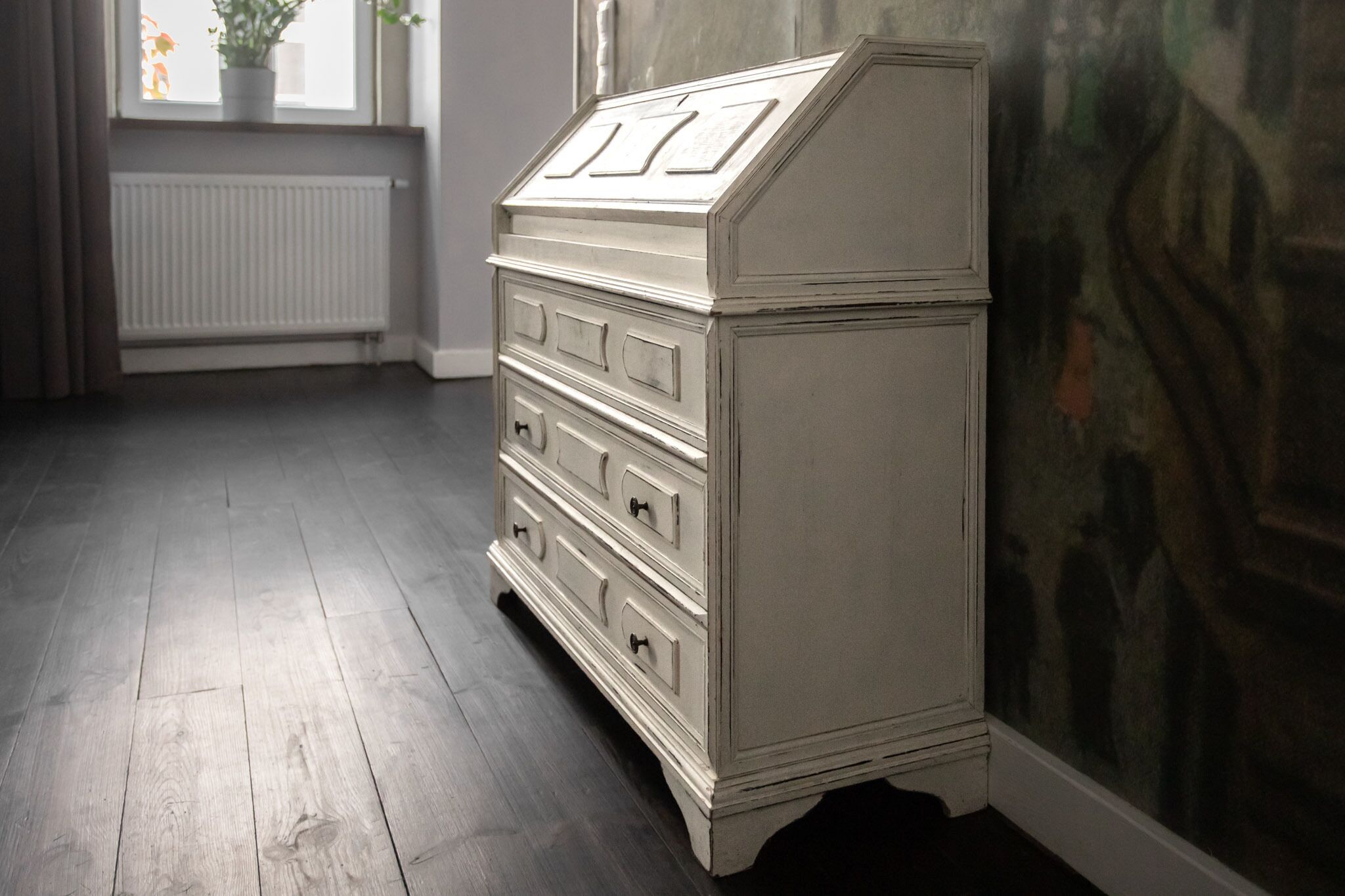 A white dresser with drawers and a top cabinet in a room with wooden flooring and a radiator.