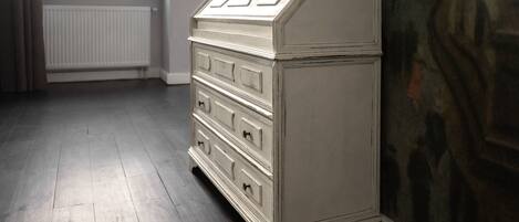 A white dresser with drawers and a top cabinet in a room with wooden flooring and a radiator.