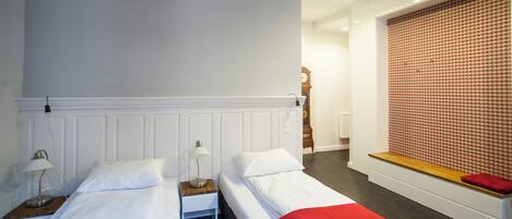 Una habitación de hotel con dos camas, un banco de madera, un papel tapiz estampado y un reloj.