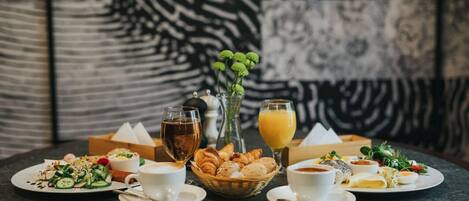 A breakfast setting with various dishes, drinks, and a vase of flowers on a table.
