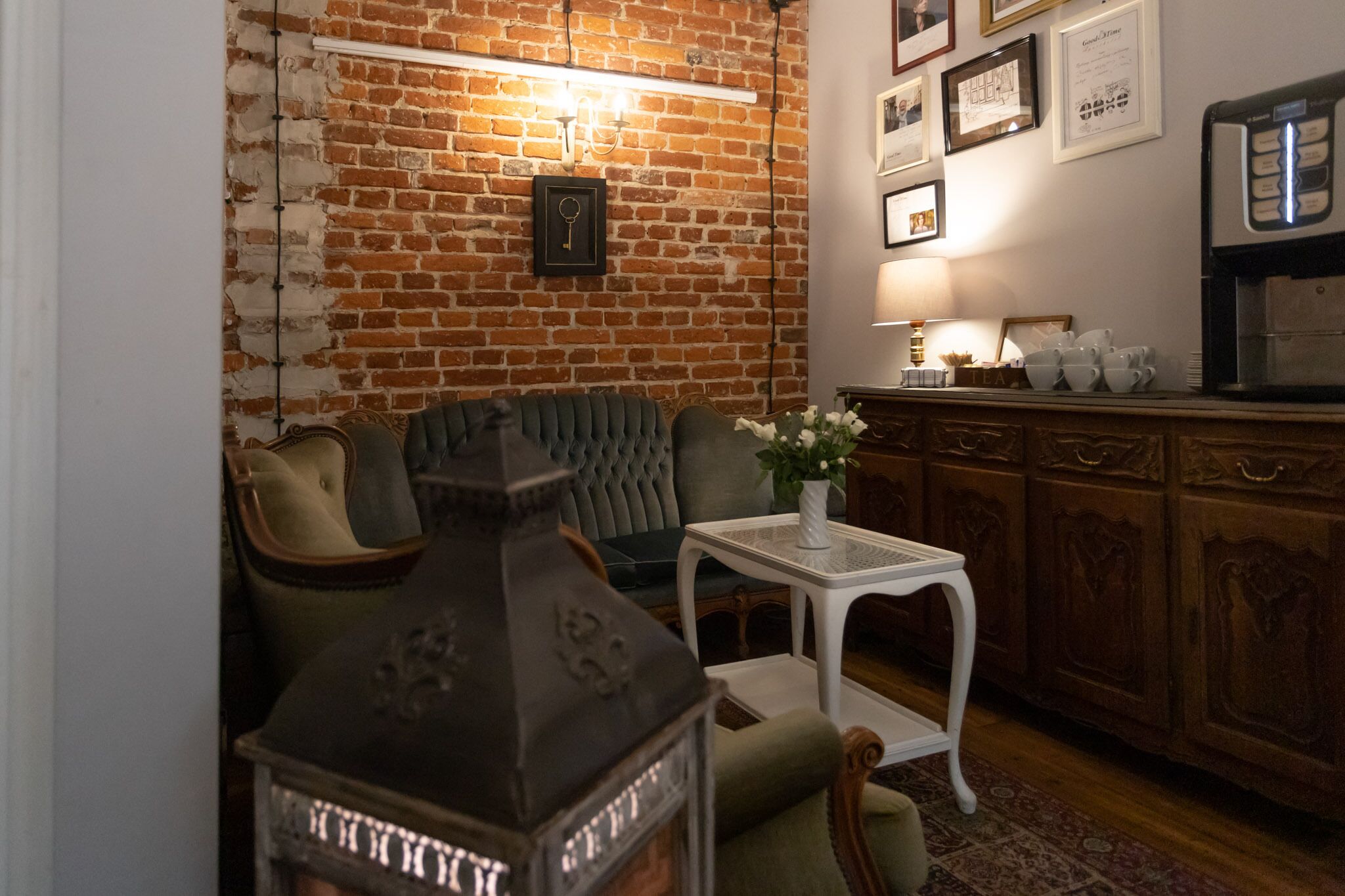 A cozy living room with a brick wall, a green sofa, a white table, and a coffee machine.