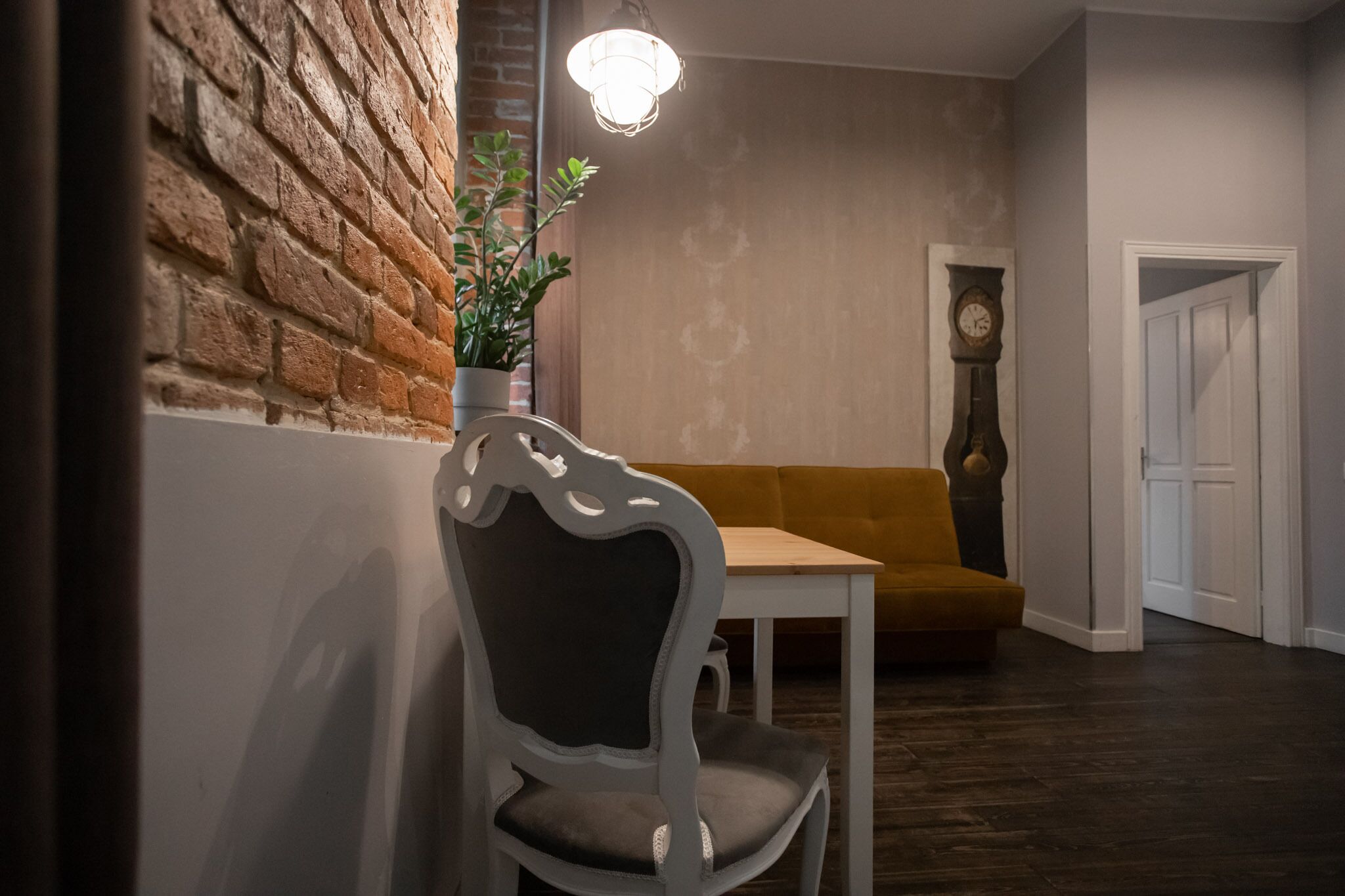 A cozy room with a brick wall, a white chair, a yellow sofa, and a wooden table.