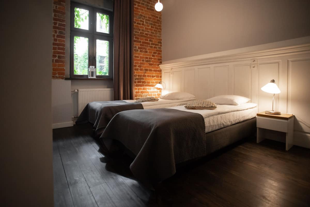 Un dormitorio con dos camas, una pared de ladrillo, una ventana y un cabecero blanco.