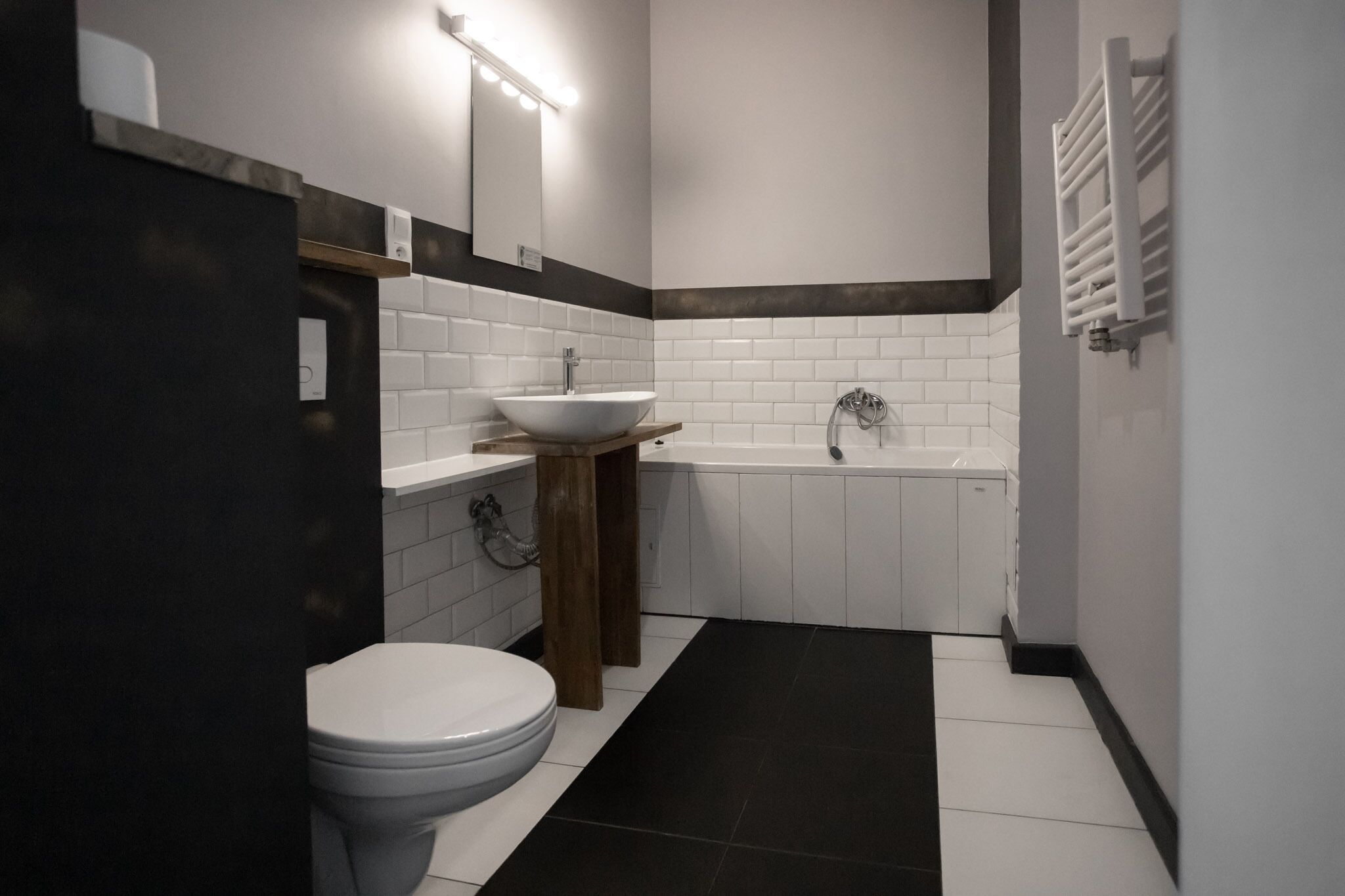 Un bany modern amb un vàter blanc, un tocador de fusta amb un lavabo blanc, una banyera i un suport per a tovalloles.