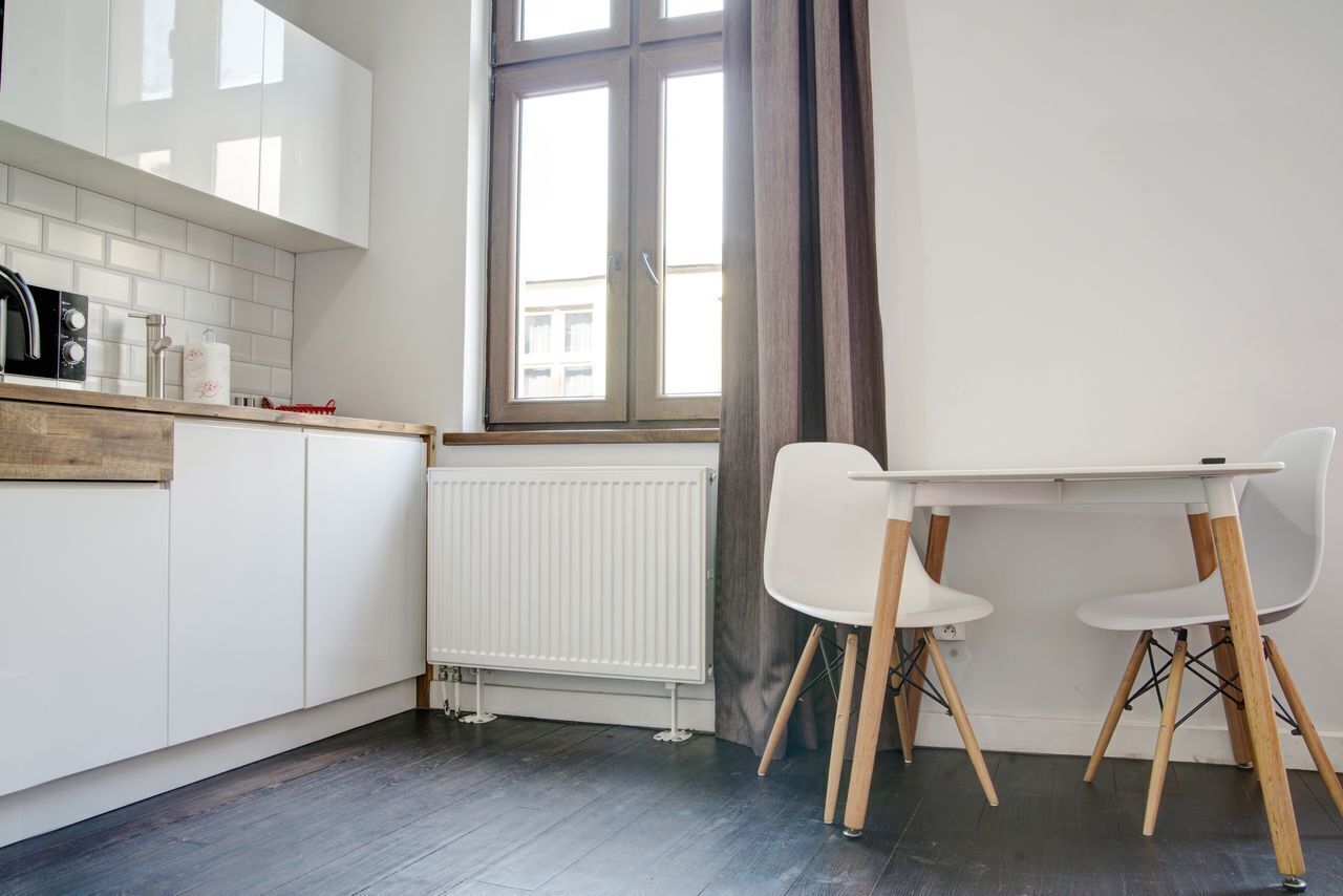 Una cocina moderna con armarios blancos, encimera de madera, una mesa blanca con dos sillas y una ventana con vistas a edificios.
