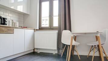 Una cocina moderna con armarios blancos, encimera de madera, una mesa blanca con dos sillas y una ventana con vistas a edificios.