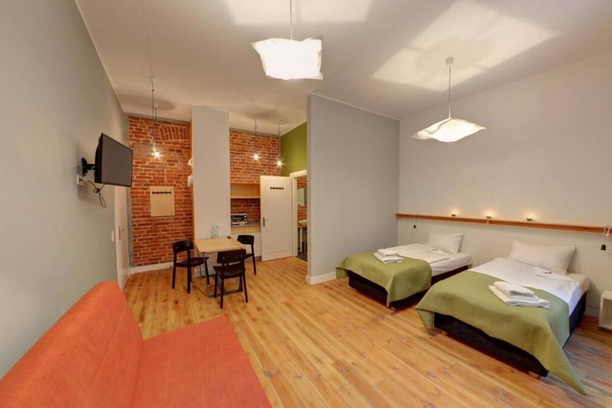 Una habitación de hotel moderna con dos camas individuales, un sofá, un comedor con mesa y sillas, y un televisor montado en la pared.