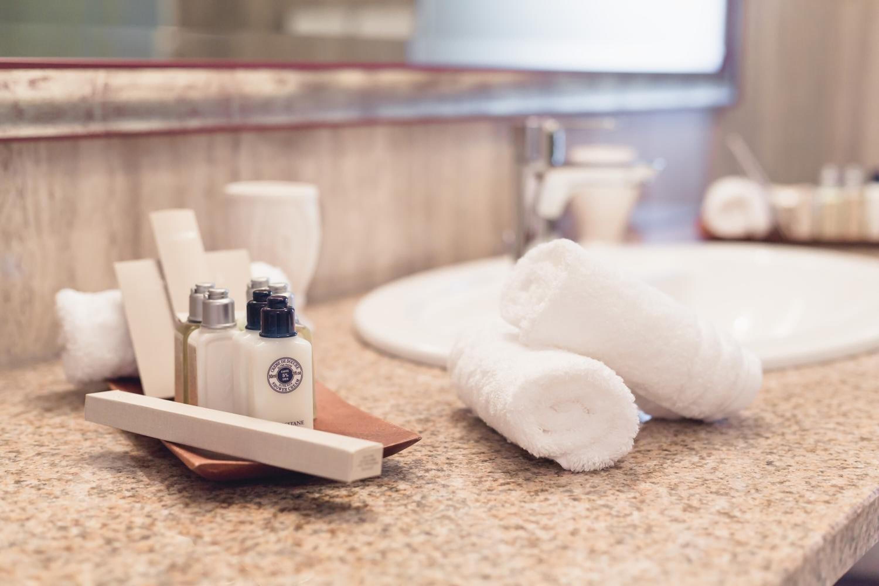 A bathroom with a granite countertop, a white sink, and toiletries including bottles and towels.