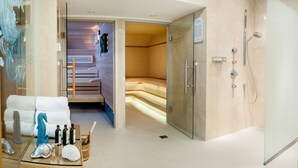 Un moderno spa con cabina de ducha de vidrio, sauna de madera y zona de relajación con sofá y elementos decorativos.