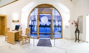 A reception area with a glass door leading to a pool, a desk with a computer, and a chair. - Schloss Thalheim (Kapelln)